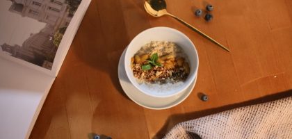 A delicious oatmeal bowl topped with nuts and mint on a wooden table.