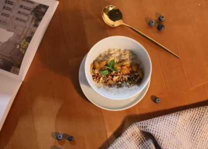 A delicious oatmeal bowl topped with nuts and mint on a wooden table.