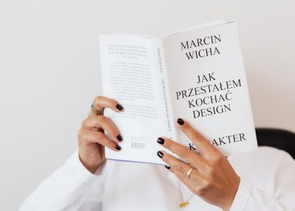 Anonymous female in white shirt with gold chain on neck reading interesting book covering face while sitting on black chair